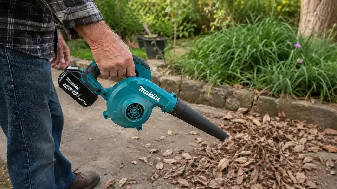 Close-up of the Makita DUB185Z cordless blower being held one-handed above a pile of dry leaves